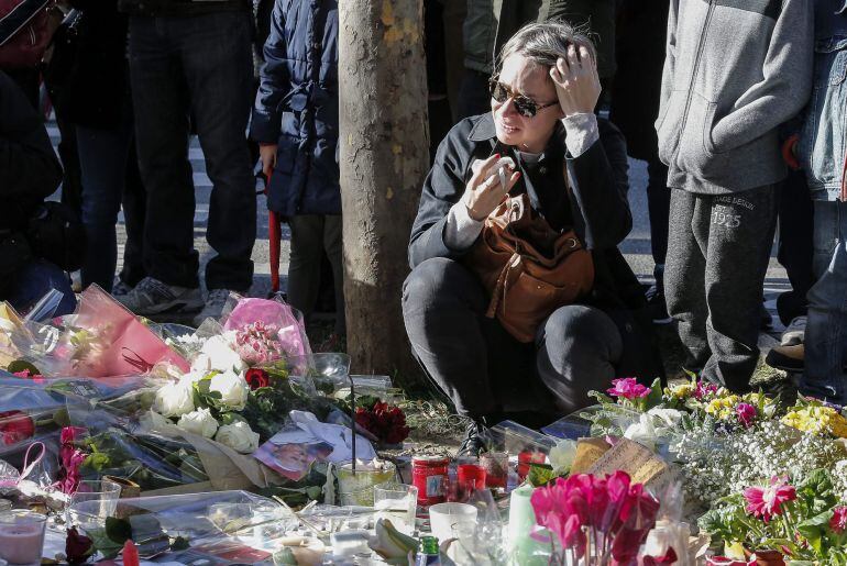 Una mujer llora tras colocar flores como homenaje a las víctimas de los atentados de París