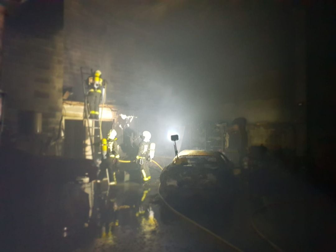 Los bomberos inspeccionan el interior del taller afectado por las llamas.