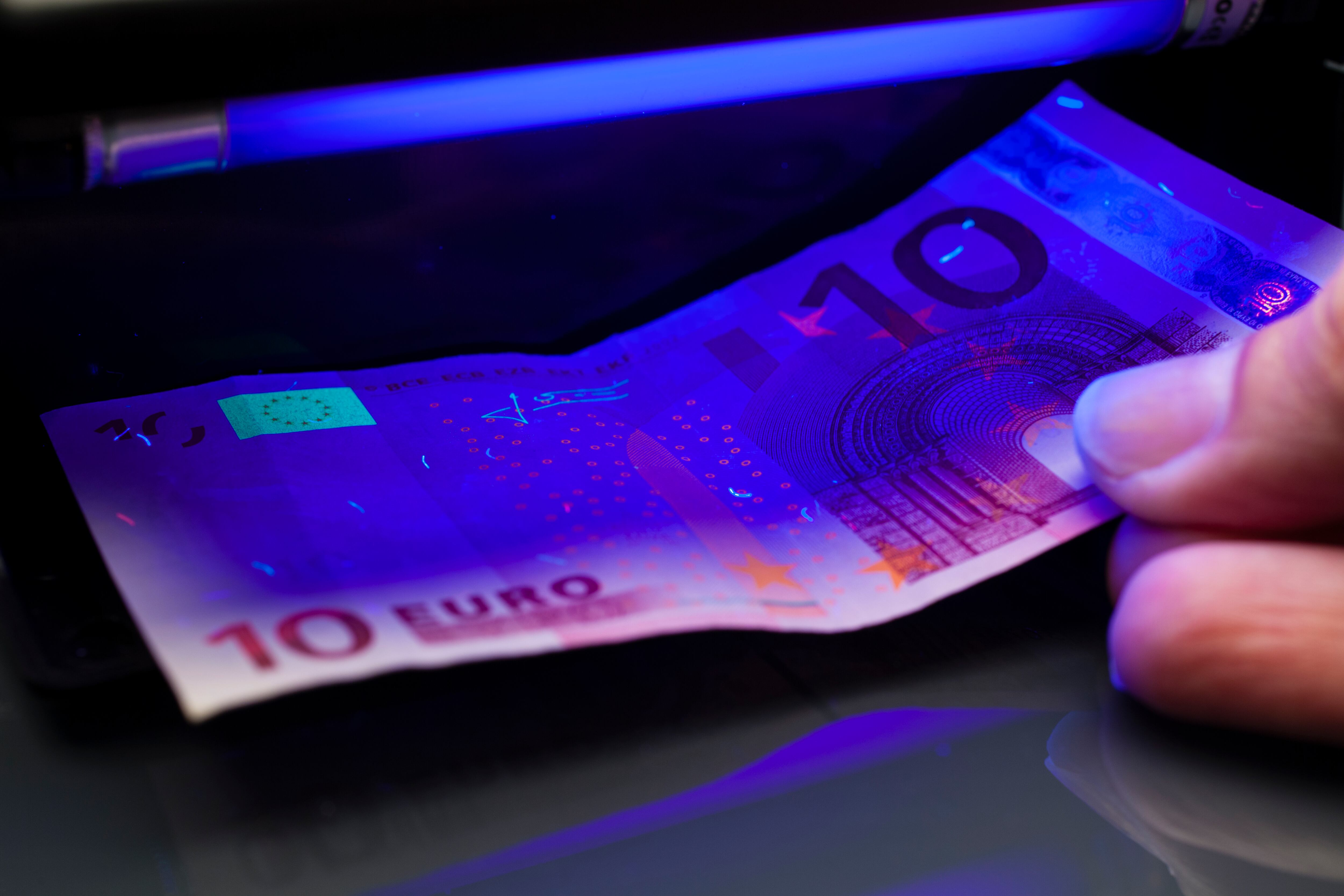 Close up photography of somebody checking a 10 euro banknote with a blacklight tester.