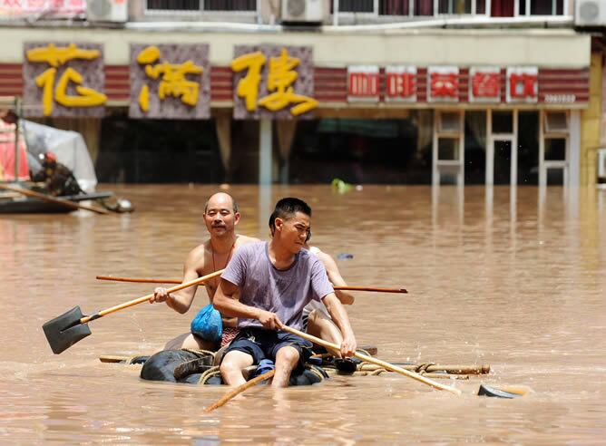 China vive sus peores inundaciones en décadas. Dos hombres reman con  palas de cavar para escapar del agua en Quxian, en la provincia de Sichuan