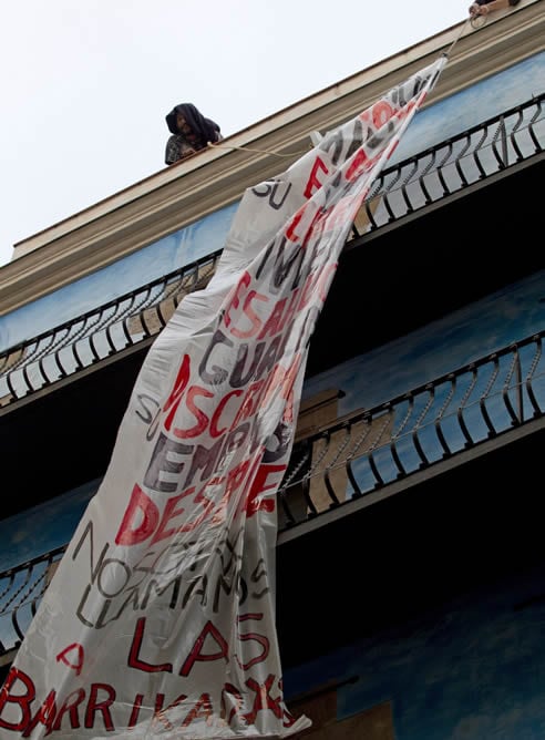 Dos manifestantes despliegan una pancanrta tras la ocupación de un bloque de pisos en el Carrer Sant Pere mes Baix