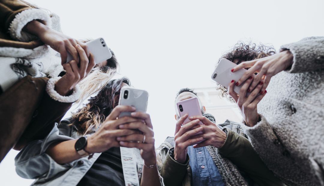 Cuatro personas consultan sus smartphones.