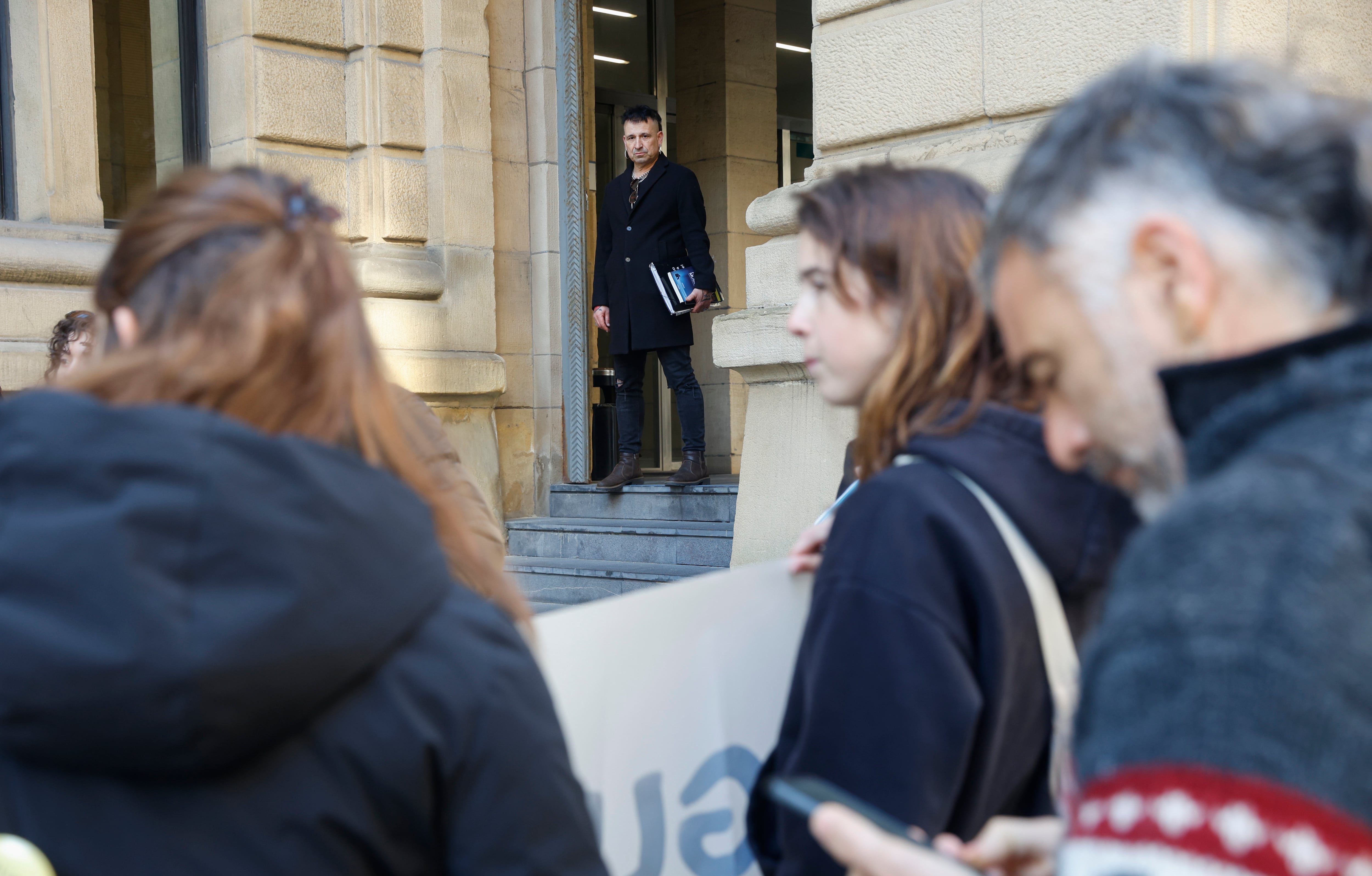 GRAFCAV1362. SAN SEBASTIÁN (ESPAÑA), 24/03/2026.- El acusado, Jon Perurena (c), observa una cocentración en su contra en la Audiencia de Gipuzkoa, antes de arrancar el juicio contra este profesor para el que la Fiscalía solicita penas que suman 22 años de cárcel, acusado de solicitar favores sexuales a tres alumnas menores de edad de un centro educativo de Irun (Gipuzkoa). EFE/ Juan Herrero