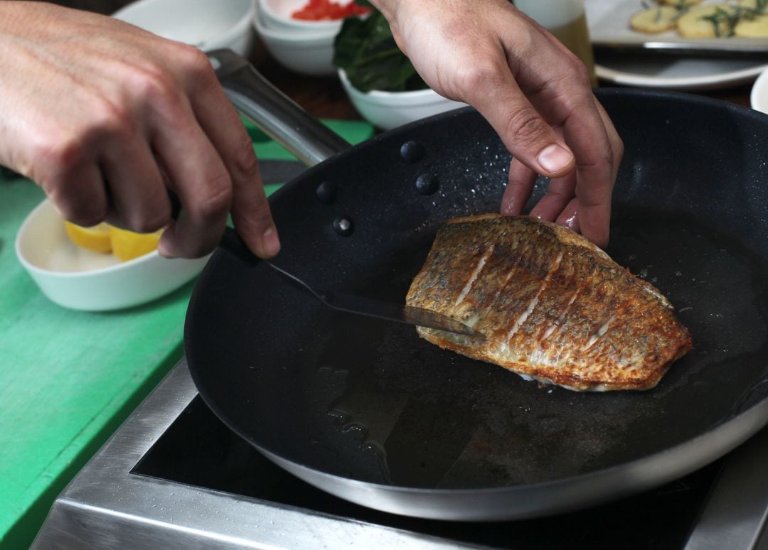 Una persona cocinando pescado a la plancha