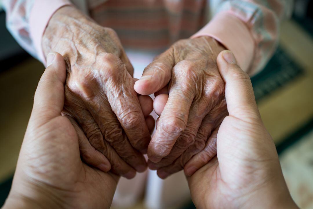 Una persona acaricia las manos de una anciana. 