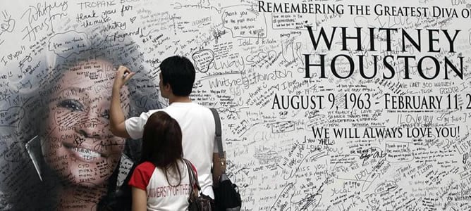 Un joven firma un mural con la fotografía de la cantante estadounidense Whitney Houston, en un centro comercial de Filipinas (EFE)