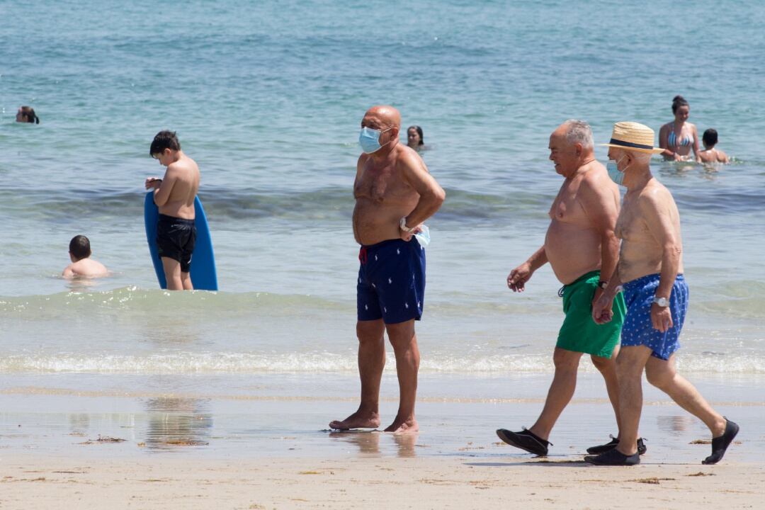 Tres hombres protegidos con mascarillas pasean por la Playa de A Rapadoira en Foz, en la comarca de A Mariña.