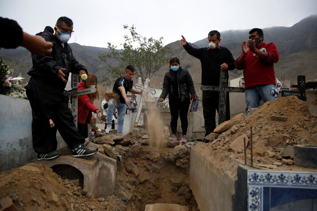 Las personas arrojan tierra sobre un ataúd durante un funeral en un cementerio en Lima