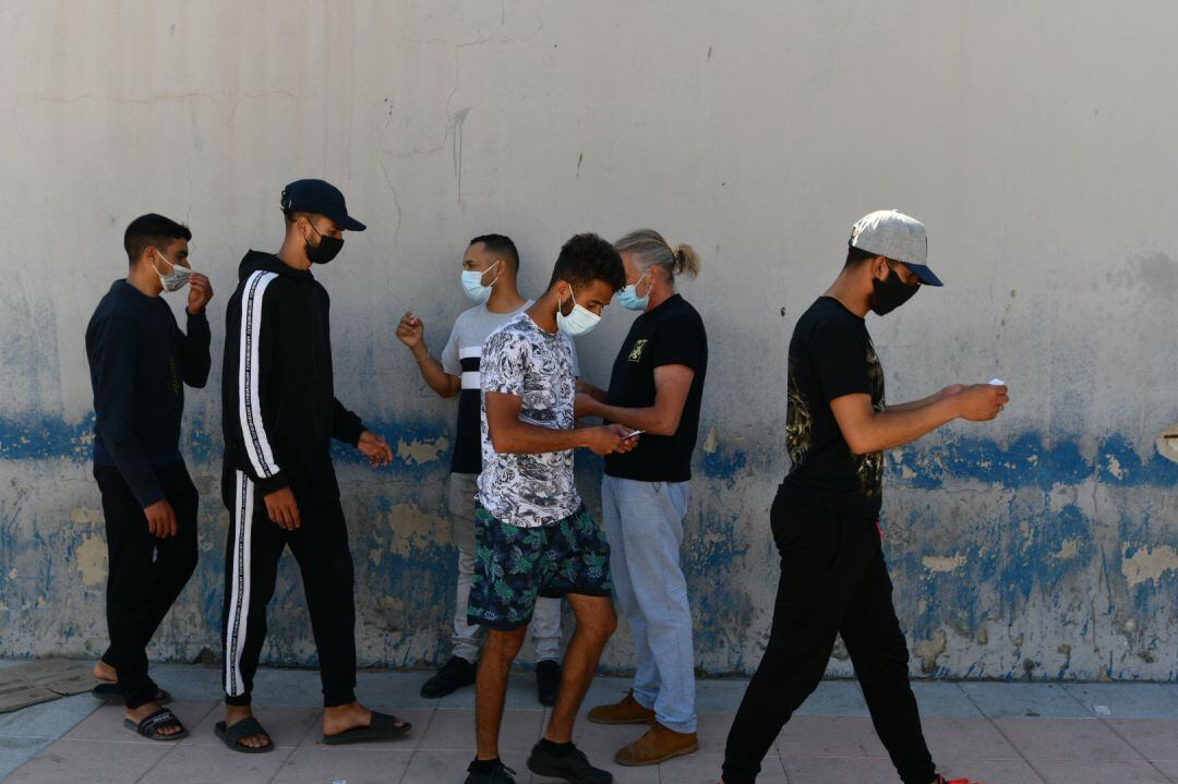 Un trabajador entrega la cita para la solicitud de asilo a varios migrantes procedentes de Marruecos que hacen cola en las puertas de la frontera de Ceuta, a 2 de junio de 2021.