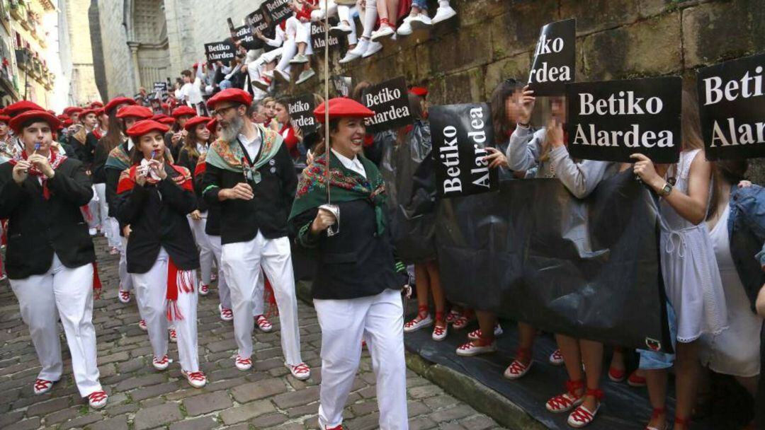 La compañía Jaizkibel, integrada por hombres y mujeres, desciende la calle Mayor ante pancartas y plasticos desplegados por seguidoras del alarde tradicional.