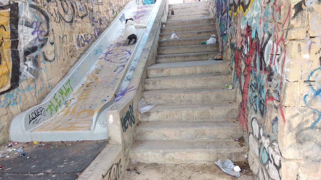 Una niña juega en un tobogán del parque Monte Tossal junto con restos de botellón y basura
