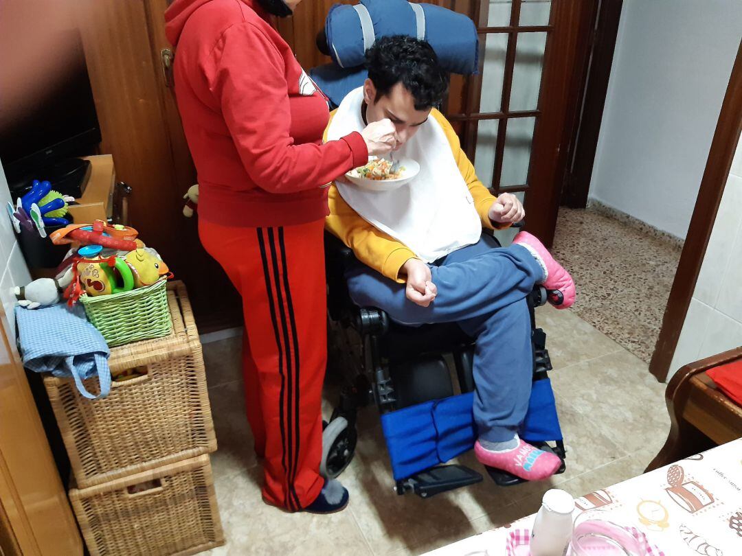 Una madre ayuda a comer a su hijo dependiente en casa.