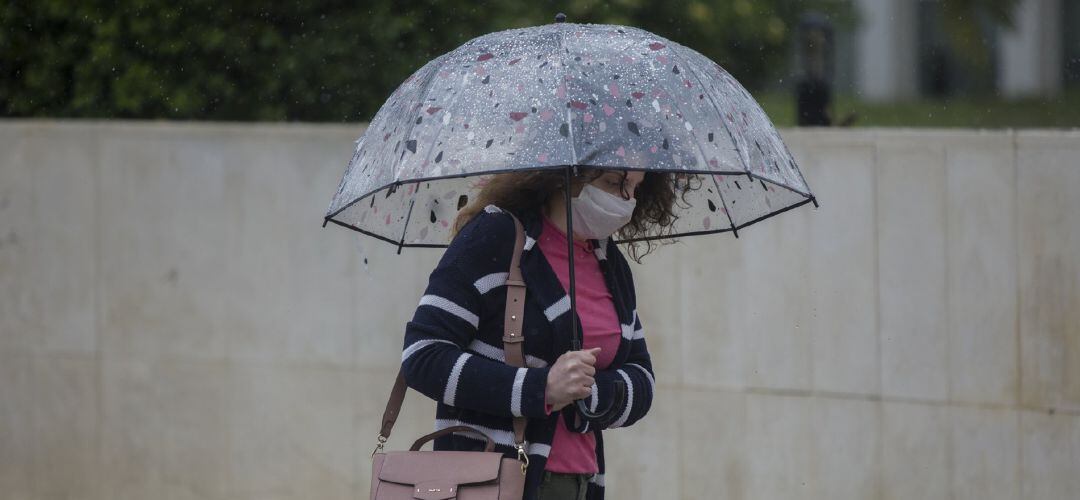 Una mujer camina bajo la lluvia con una mascarilla quirúrgica.