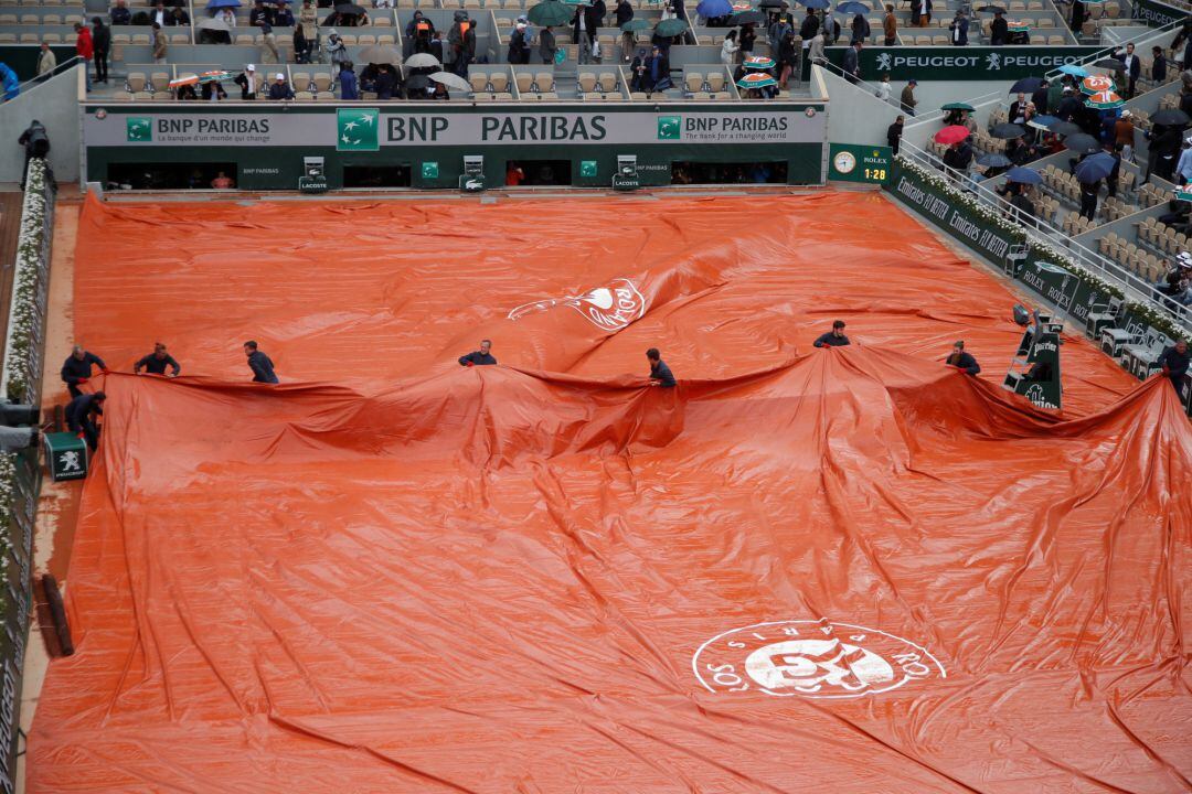 La organización del torneo pone la lona para evitar que se moje la tierra batida de la pista central de Roland Garros tras suspenderse el Djokovic - Thiem en el tercer set