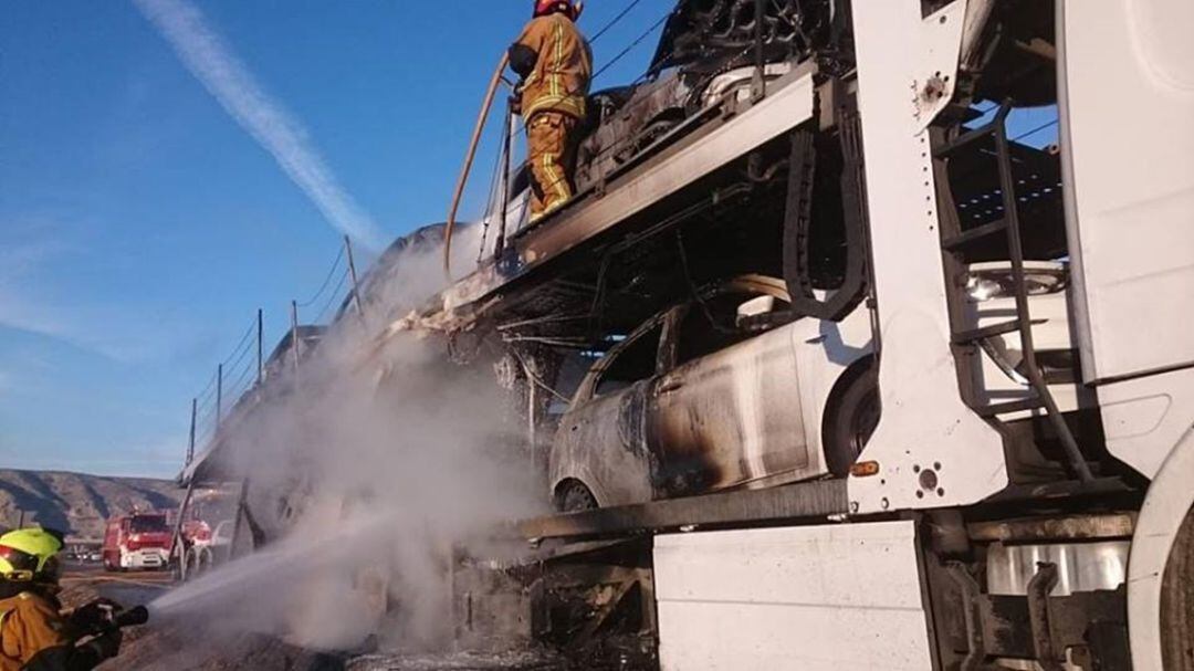 Efectivos del Consorcio Provincial de Bomberos de Alicante extinguen las llamas en un camión que transportaba siete automoviles