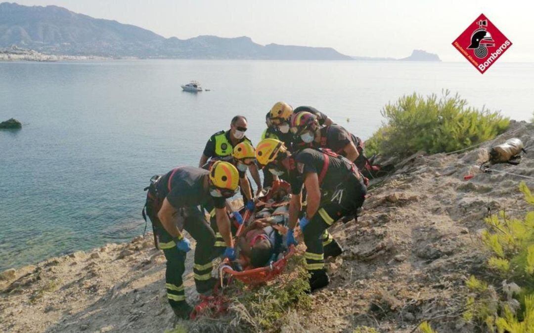 Varios bomberos colocan en una camilla a la mujer herida, traes caer por un acantilado de l'Alfàs del Pi.