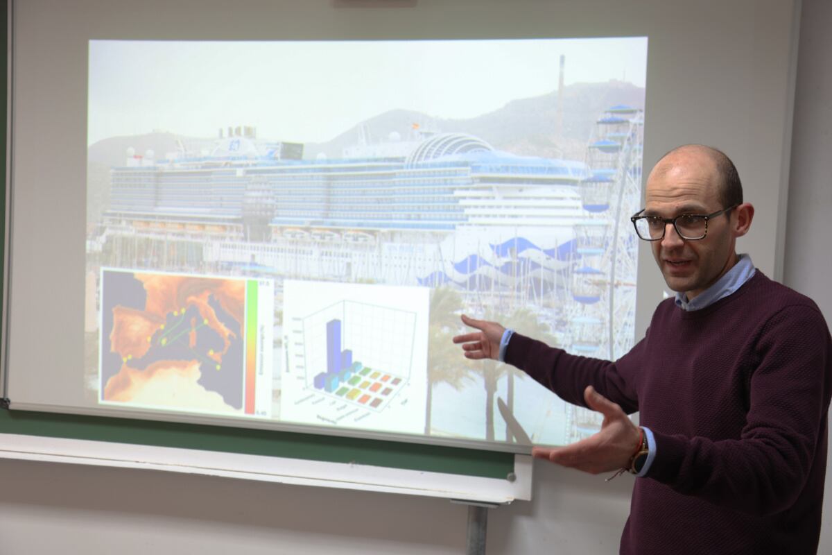 Jerónimo Esteve mostrando gráficas de la reducción de emisiones y las rutas más transitadas sobre una foto de un crucero moderno que hizo escala en Cartagena