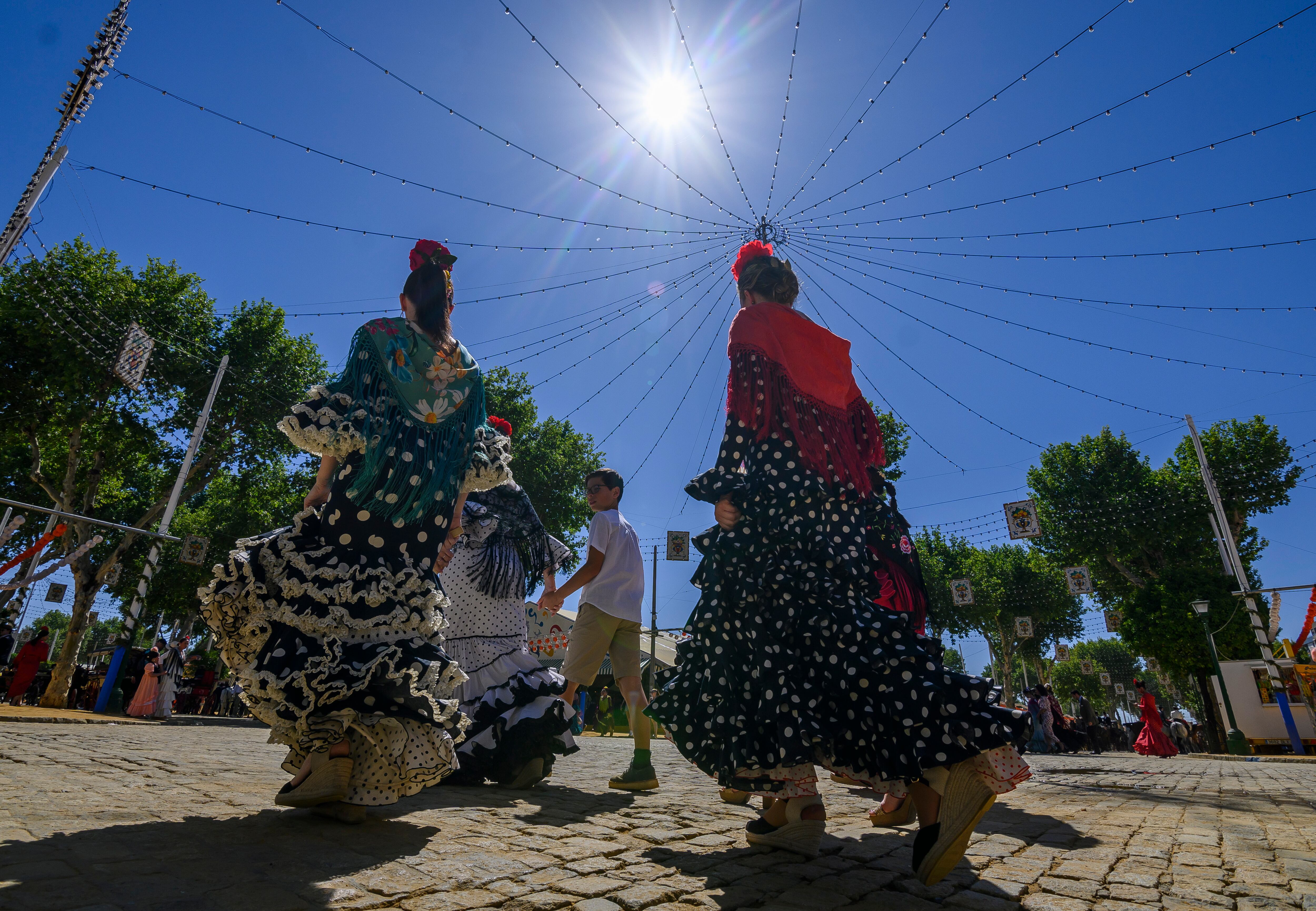 Unas mujeres vestidas de flamenca caminan por el Real de la Feria de Abril de Sevilla con temperaturas más altas de lo normal para estas fechas. EFE/Raúl Caro