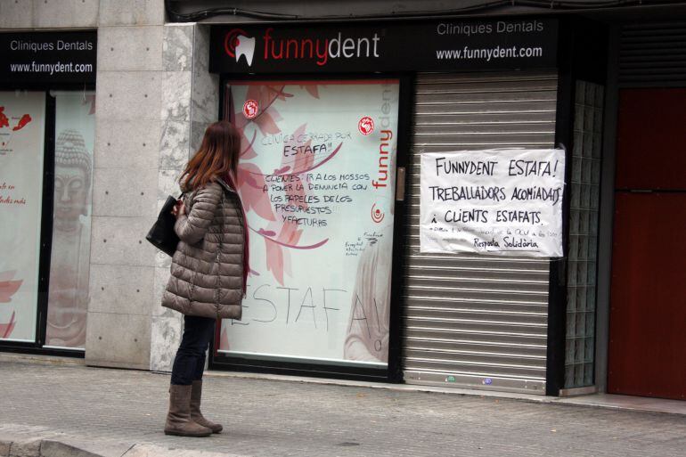 Una noia mira les pancartes de protesta a l&#039;aparador de la clínica dental Funnydent, a Mataró. Imatge del 29 de gener de 2016. (Horitzontal)