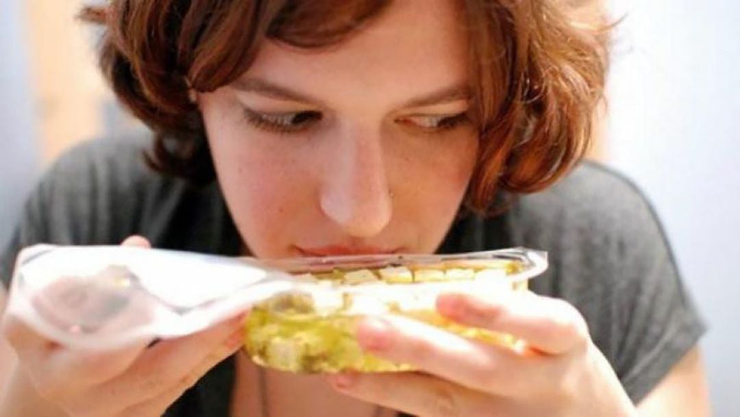 Una mujer huele un envase con comida