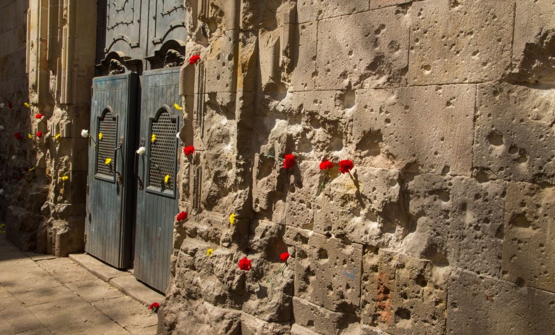 Fachada de la iglesia de Sant Felip Neri con todas las &#039;cicatrices&#039; producidas durante los bombardeos de la Guerra Civil española en el antiguo barrio de la ciudad de Barcelona, ​​decorada con claveles