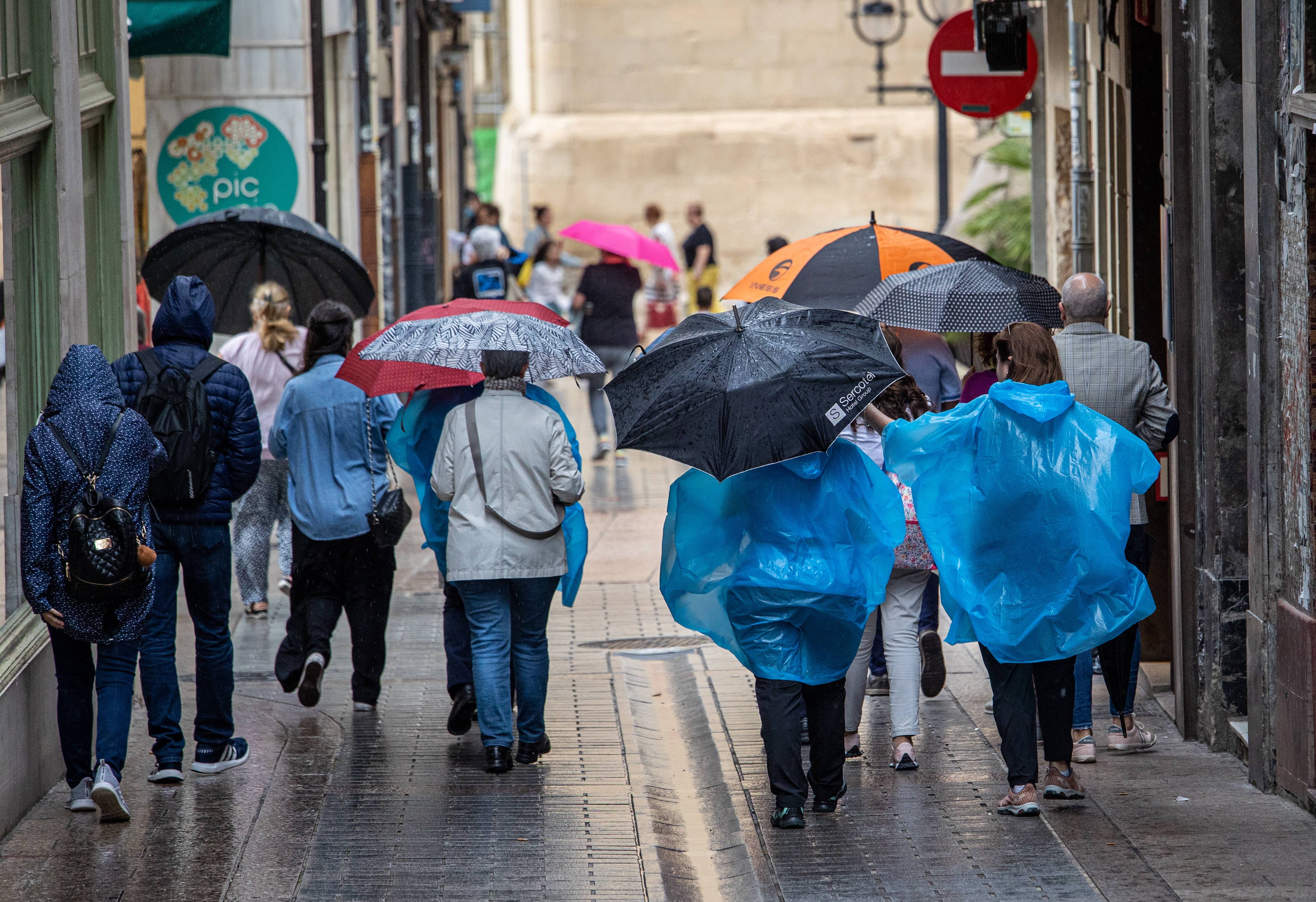 Turistas y transeuntes caminan bajo la lluvia