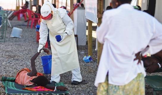 A health worker wearing protective equipment assists an Ebola patient at the Kenama treatment centre run by the Red Cross Society on November 15, 2014. Ebola-hit Sierra Leone faces social and economic disaster as gains made since the country&#039;s ruinous civ