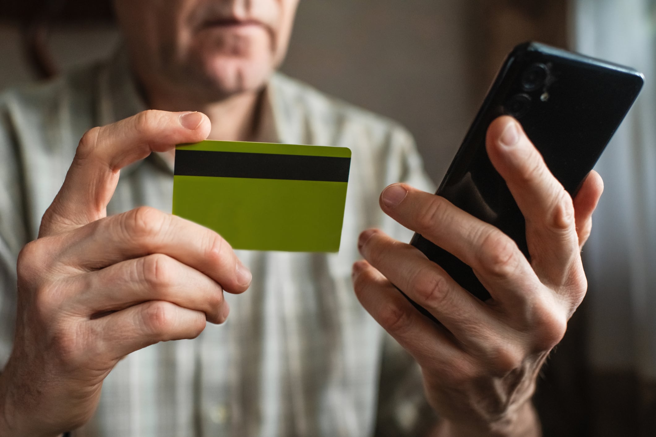 Un hombre mayor consulta su tarjeta de crédito mientras habla por teléfono.