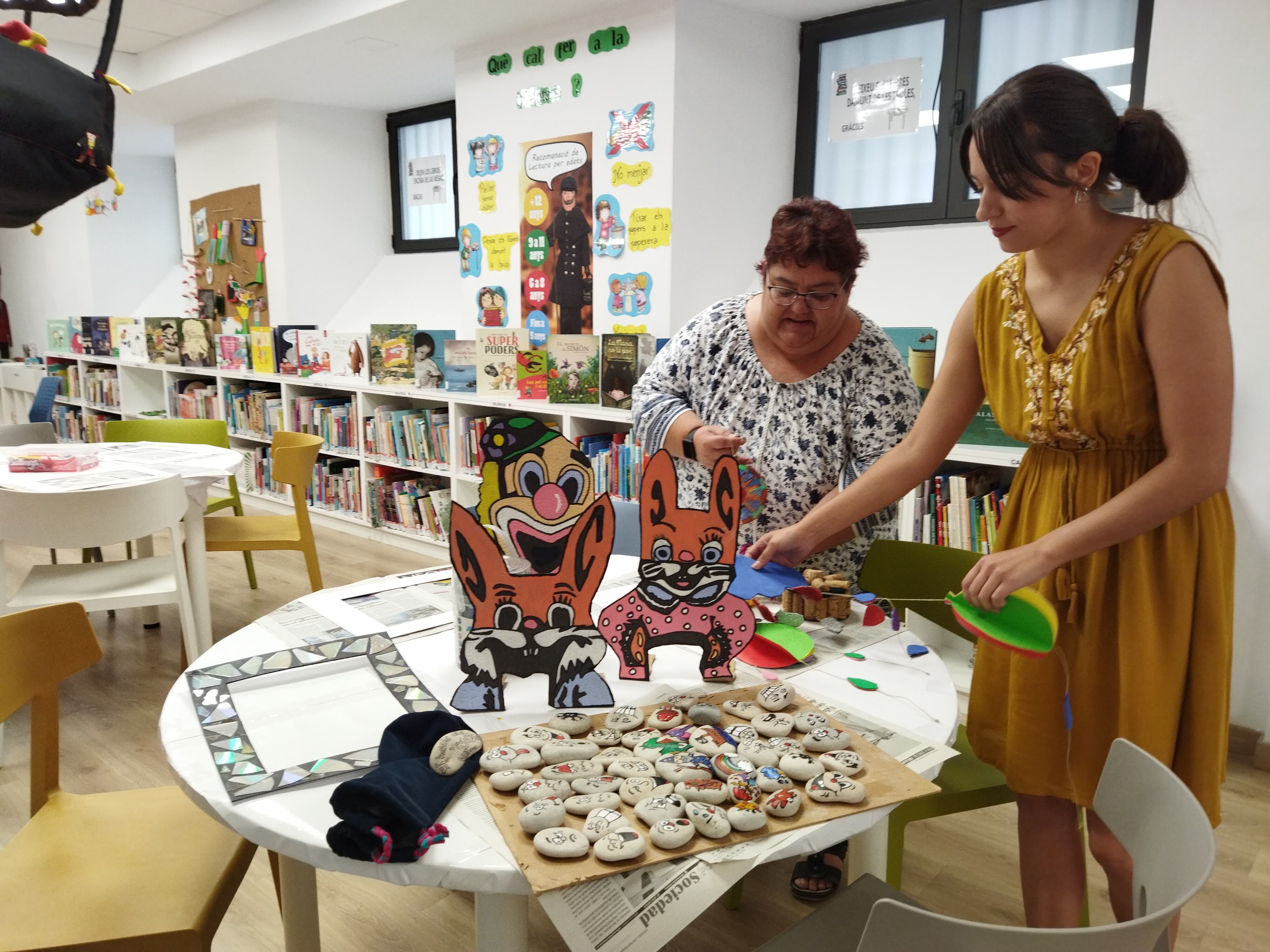 Sari Sanchis i Nerea Gil, tècniques d'animació sociocultural, en la biblioteca de Tirisiti amb les manualitats que es faran als tallers d'aquest estiu.