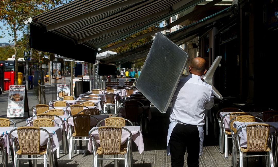 Un camarero recoge una mesa de una terraza de un restaurante del barrio de la Barceloneta de Barcelona.