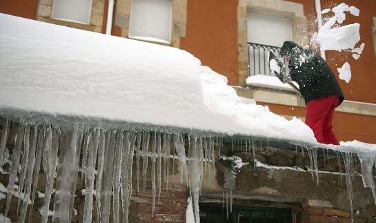 Un hombre quita la nieve del tejado de su casa en la localidad cántabra de Reinosa