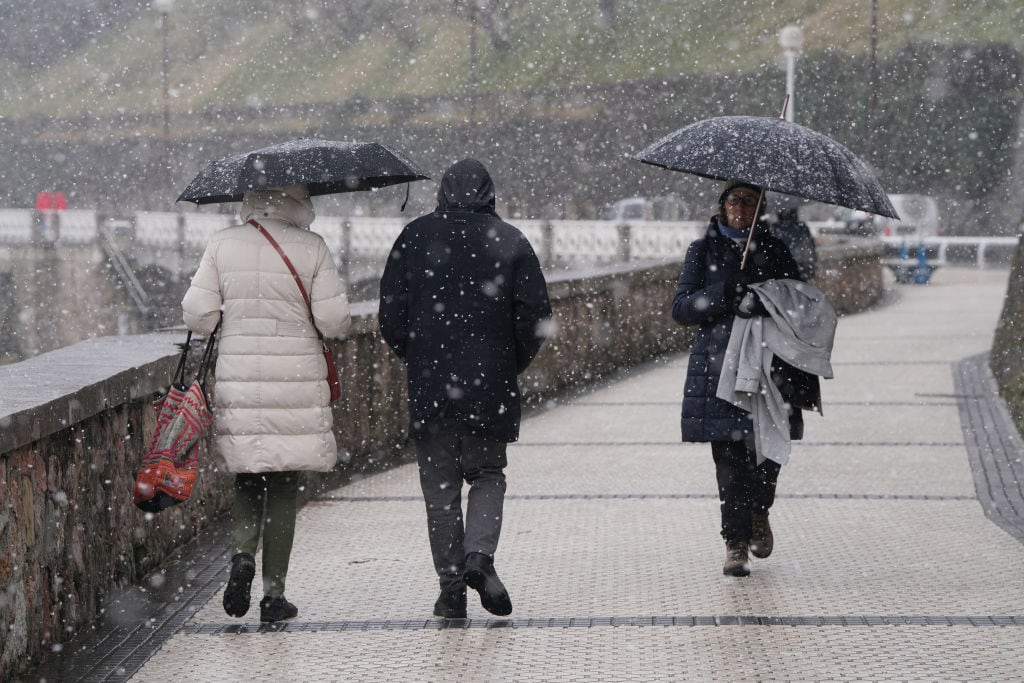 Viandantes pasean bajo la nieve en San Sebastián.