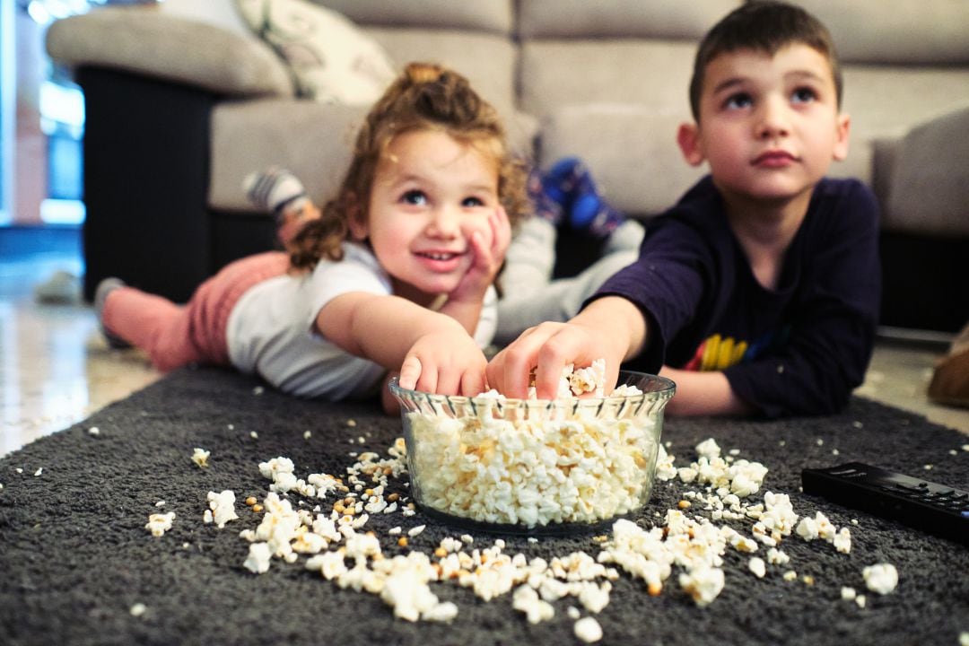 Niños viendo la tele mientras comen palomitas.