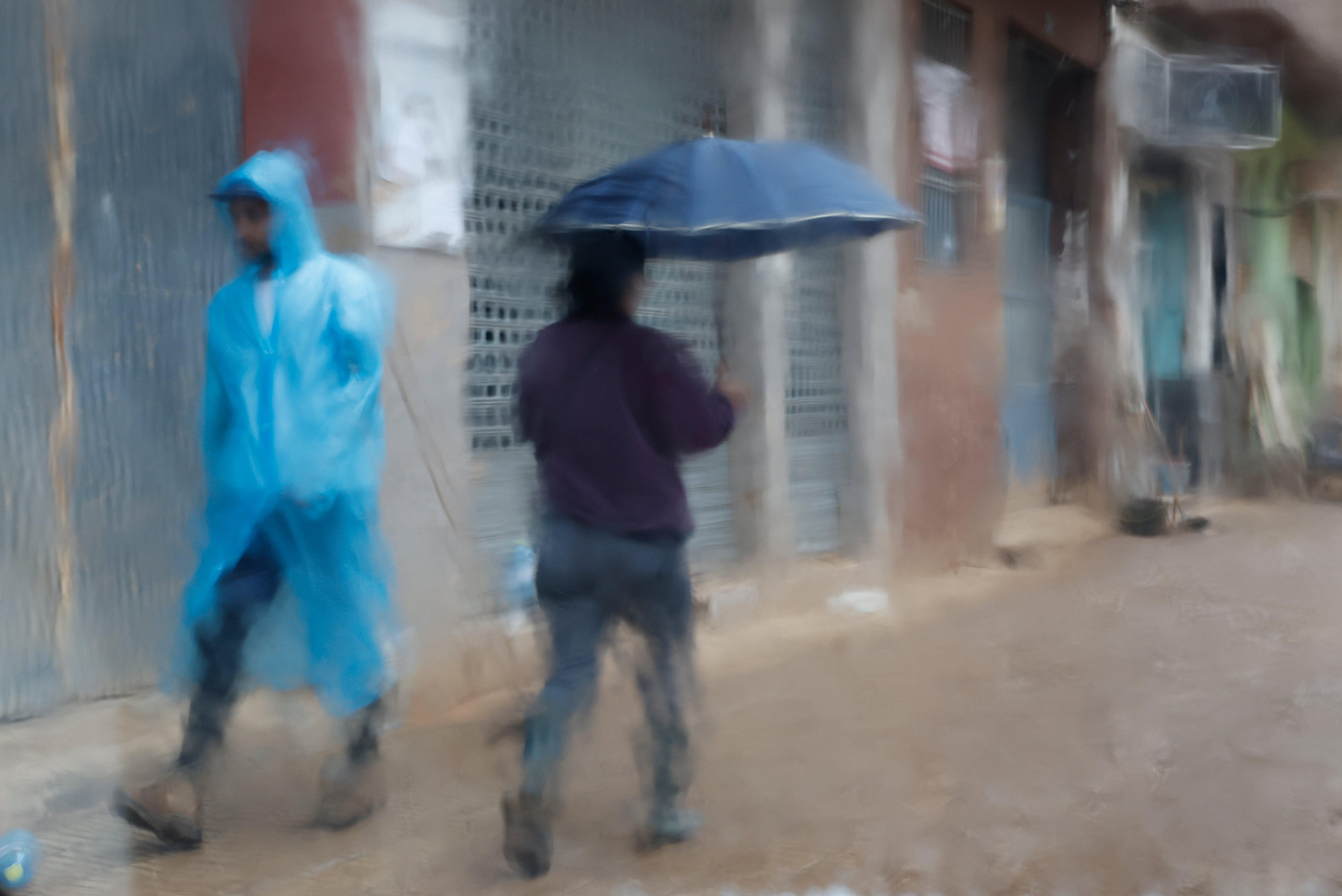 Fotografía tomada tras un cristal de dos personas que caminan protegida para la lluvia por Paiporta (Valencia) este miércoles