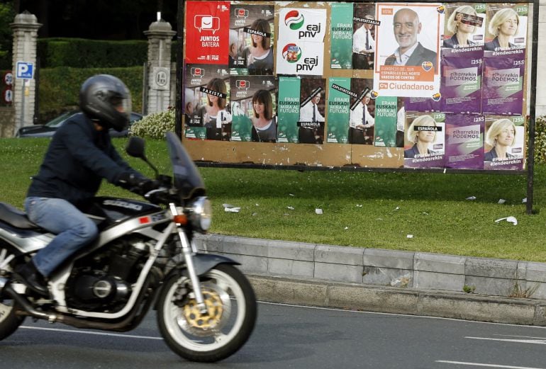 Un motorista pasa ante una valla con los candidatos a lehendakari en una calle de Bilbao 