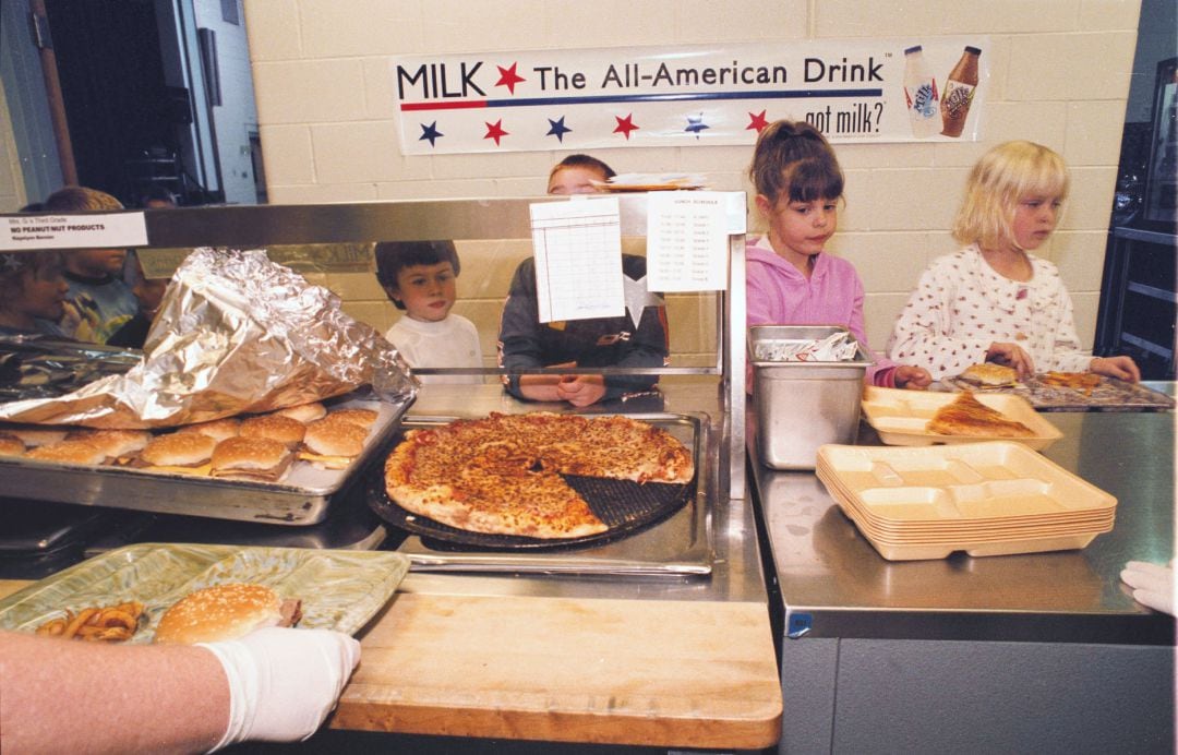 Unos niños esperan para recoger su comida en un comedor escolar de Estados Unidos en 2002. En las vitrinas, pizzas y hamburguesas con patatas.