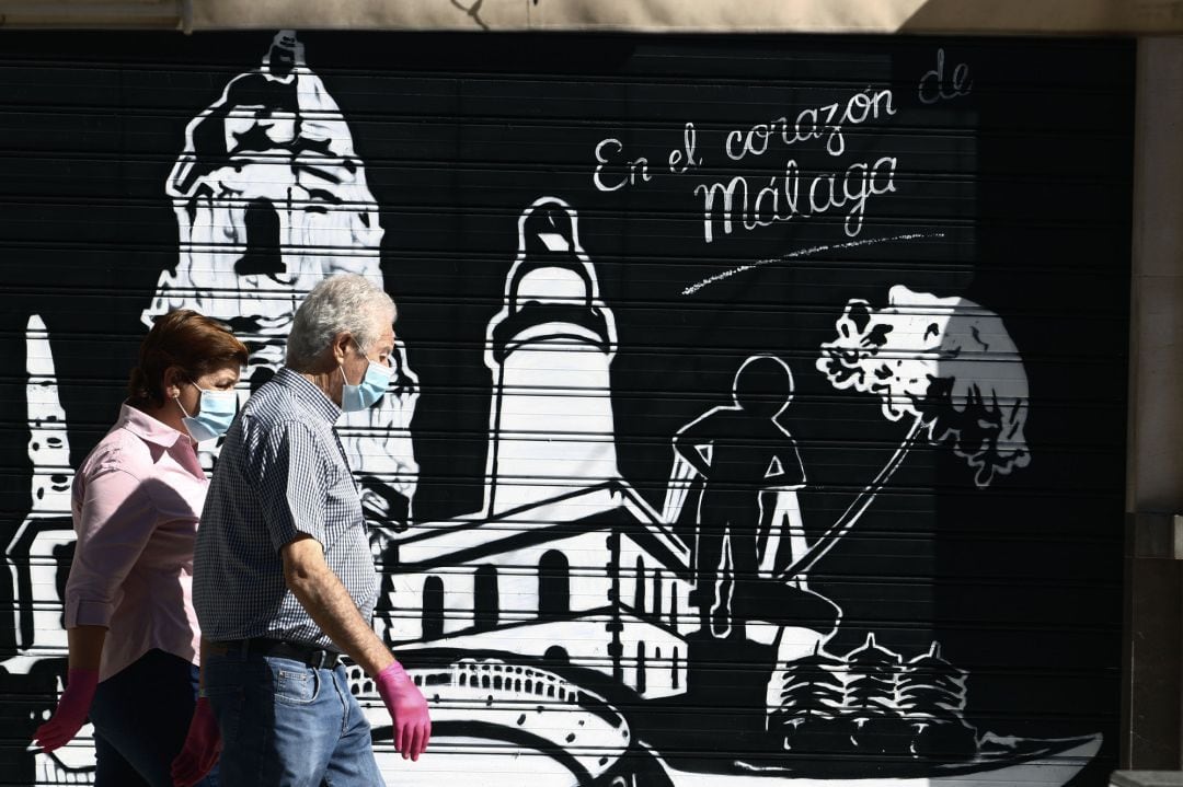 Dos personas caminan juntas en Málaga, donde van protegido por mascarillas y guantes por el virus COVID-19