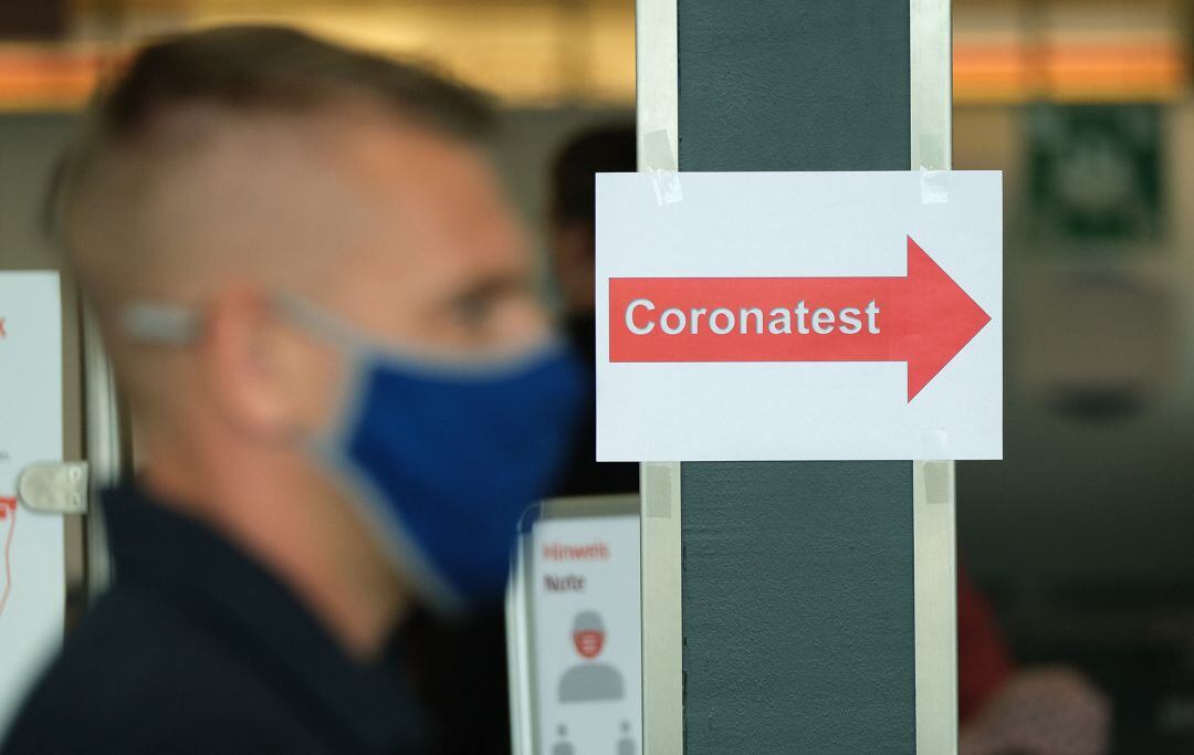 Un hombre con mascarilla junto a un cartel que indica que se realizan test de coronavirus.