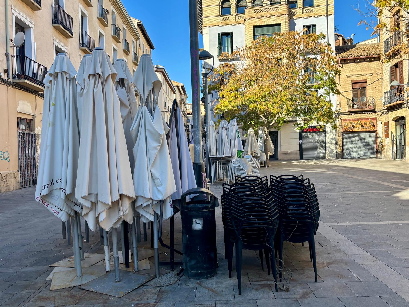 Plaza de Alfonso el Batallador repleta de sillas, mesas y sombrillas apiladas con los bares cerrados