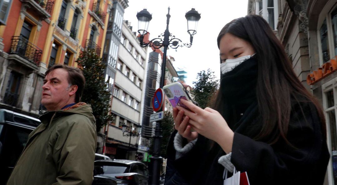 Una mujer asiática consulta su móvil protegida con una mascarilla.