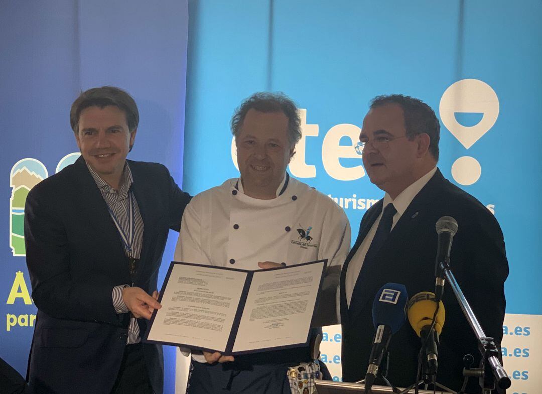 El Cofrade Mayor de la Cofradía de El Desarme, Miguel Ángel de Dios, recibe la declaración de manos del Consejero de Empleo, Industria y Turismo, Isaac Pola (Derecha), acompañado del presidente de OTEA, José Luis Álvarez Almeida (Izquierda)