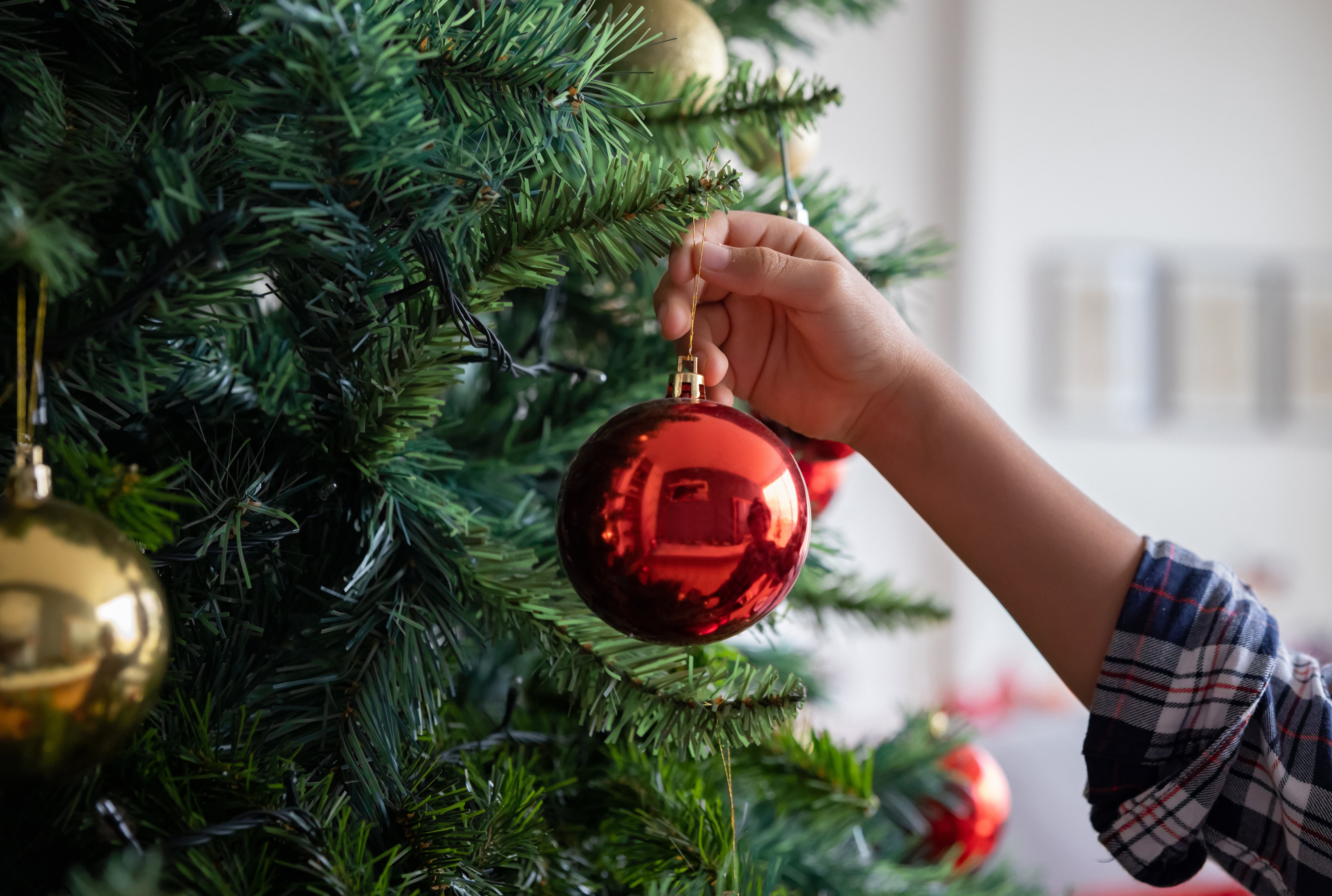 Un niño poniendo una bola de Navidad en el árbol.