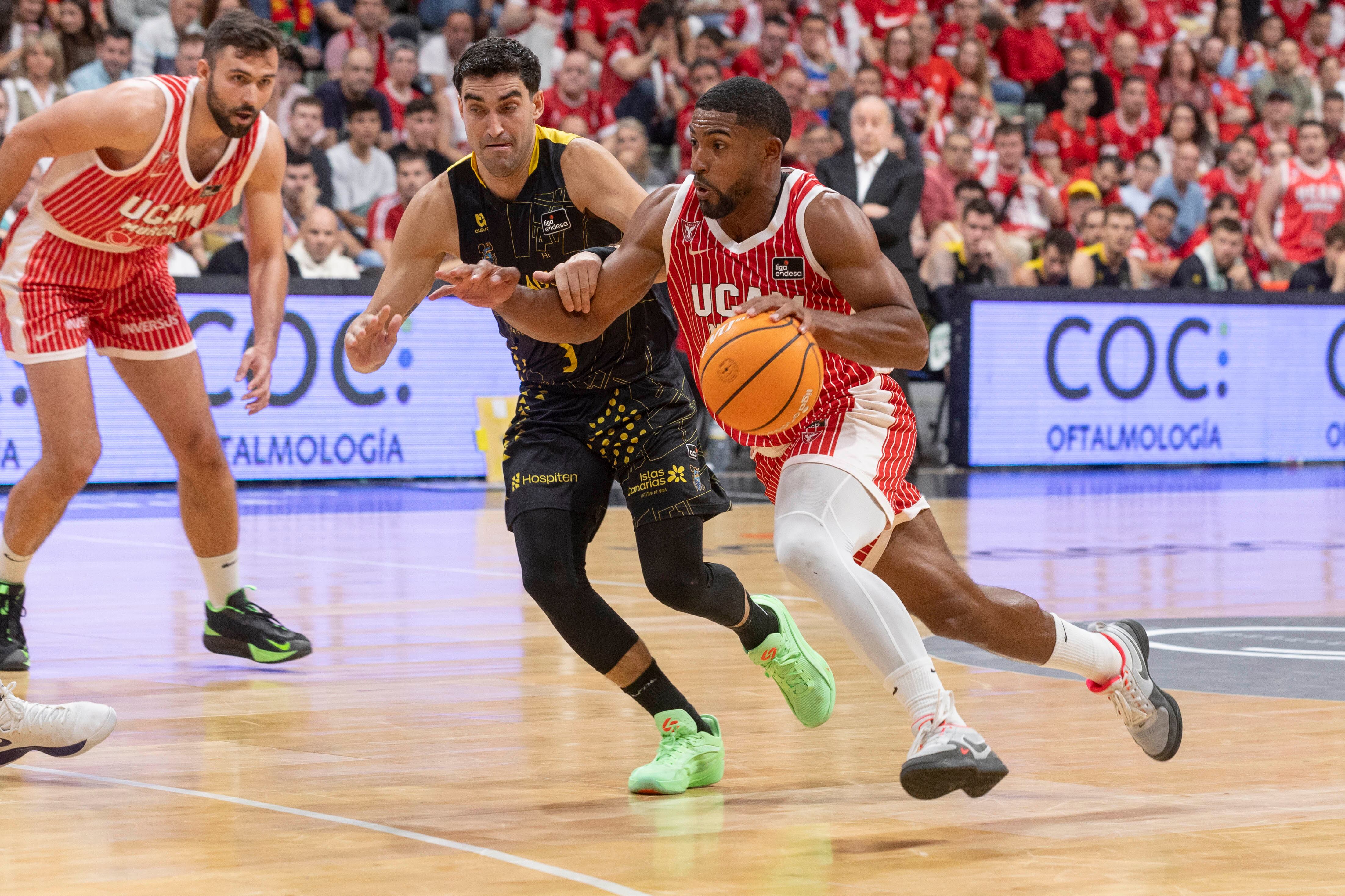 MURCIA, 25/04/2026.- El base estadounidense de UCAM Murcia David DeJulius (d), controla en balón ante la presión del escolta de La Laguna Tenerife Jaime Fernández (c), durante el partido de la vigésima octava jornada de la liga Endesa que están disputando este sábado en el Palacio de los Deportes de Murcia. EFE/Marcial Guillén