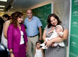 María José, en brazos de su madre, mira atentamente a la Consejera de Salud, María Jesús Montero