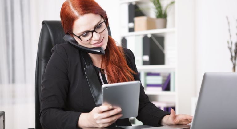 Una joven habla por teléfono, lee en la tablet y trabaja en el ordenador.