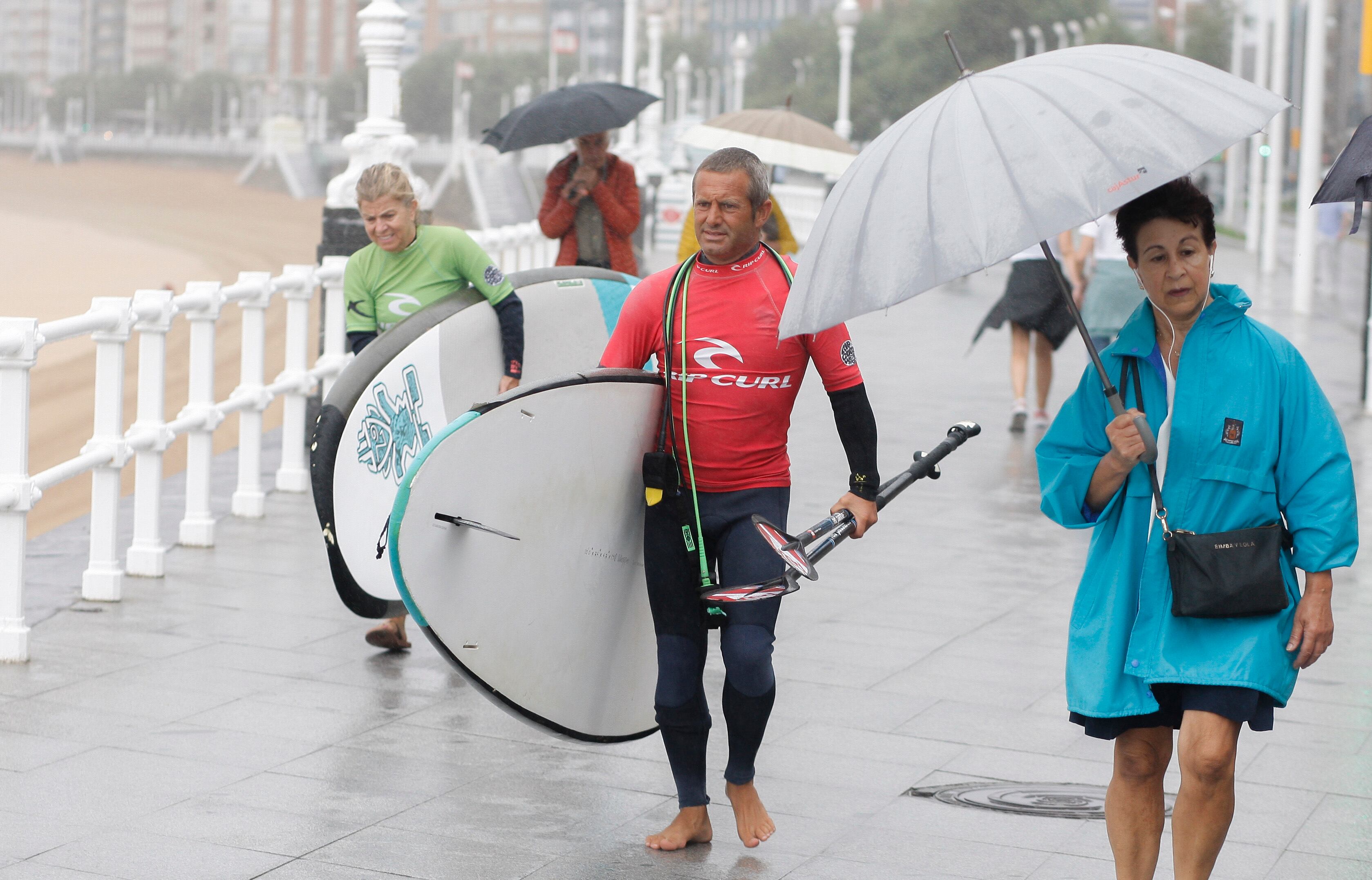 Surfistas bajo la lluvia en el Paseo Marítimo de San Lorenzo, en Gijón.