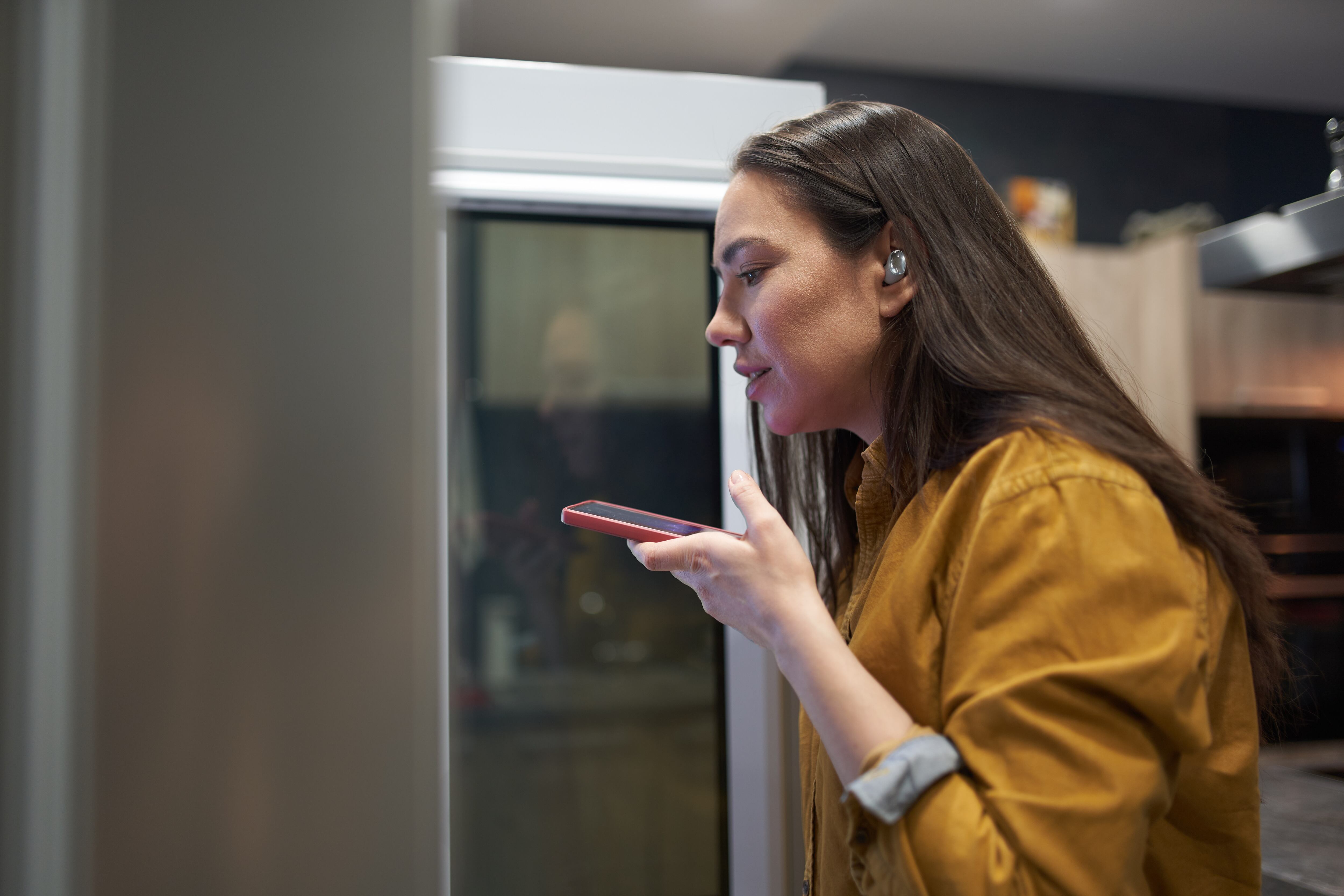 Una mujer enviando un audio mientras abre el frigorífico.