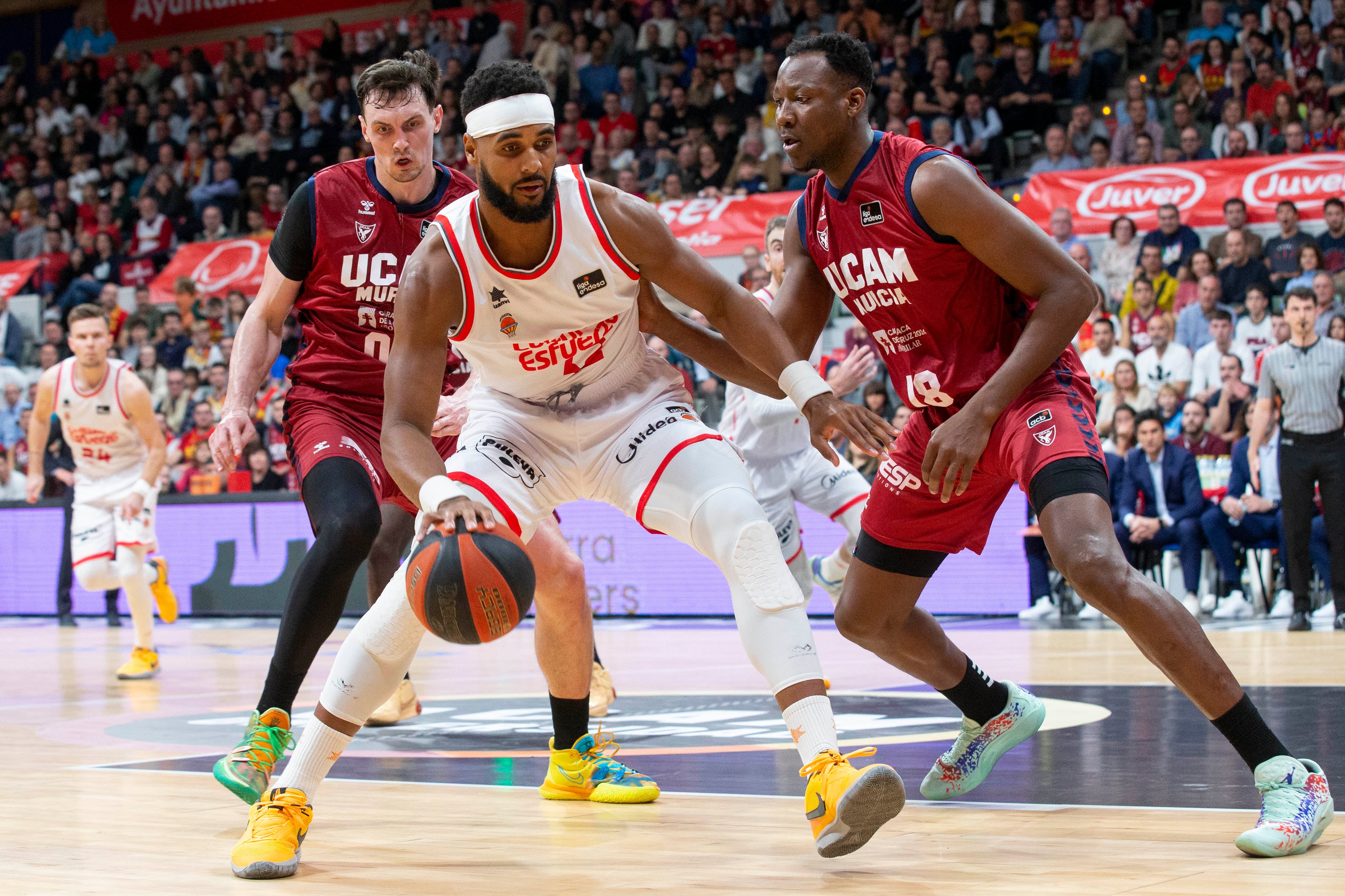 MURCIA, 10/12/2023.- El pívot ugandés de Valencia Basket Brandon Davies (c) controla el balón ante la presión del pívot congolés de UCAM Murcia Jordan Sakho (d), ante la mirada de Rodions Kurucs durante el partido de la décimo tercera jornada Liga Endesa, que están disputando este domingo en el Palacio de los Deportes de Murcia . EFE/Marcial Guillén