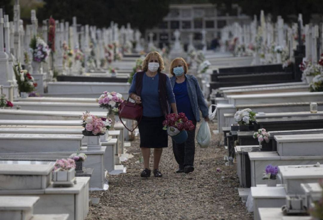Dos mujeres acuden a un cementario a depositar ramos de flores.