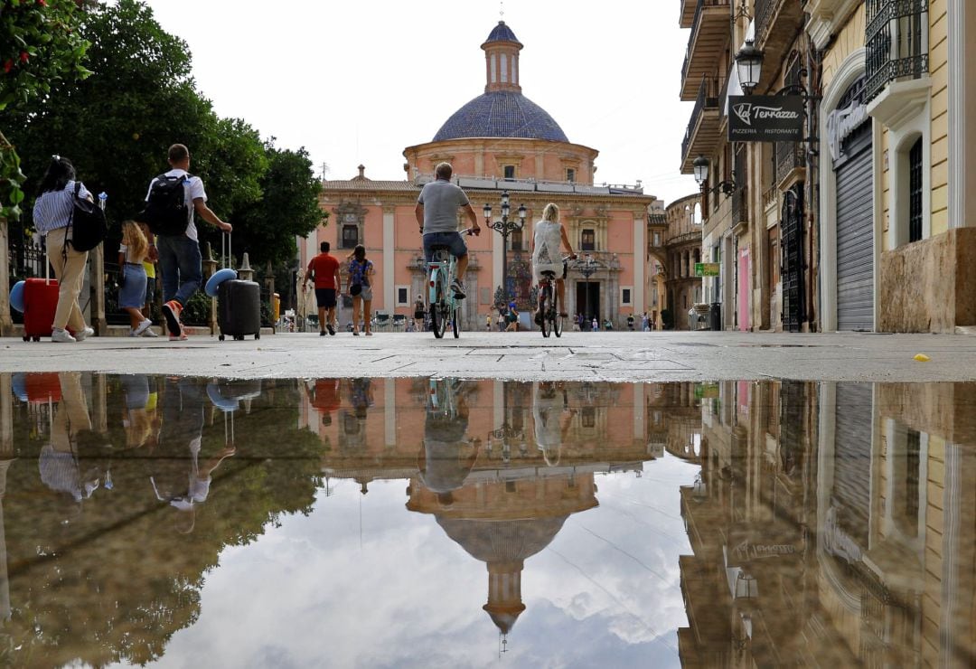 Varios turistas pasean en bicicleta mientras otros acarrean sus maletas por la plaza de la Virgen de Valencia, en el centro histórico de la ciudad. El gasto medio diario de los turistas internacionales se ha disparado al inicio de este verano en relación 